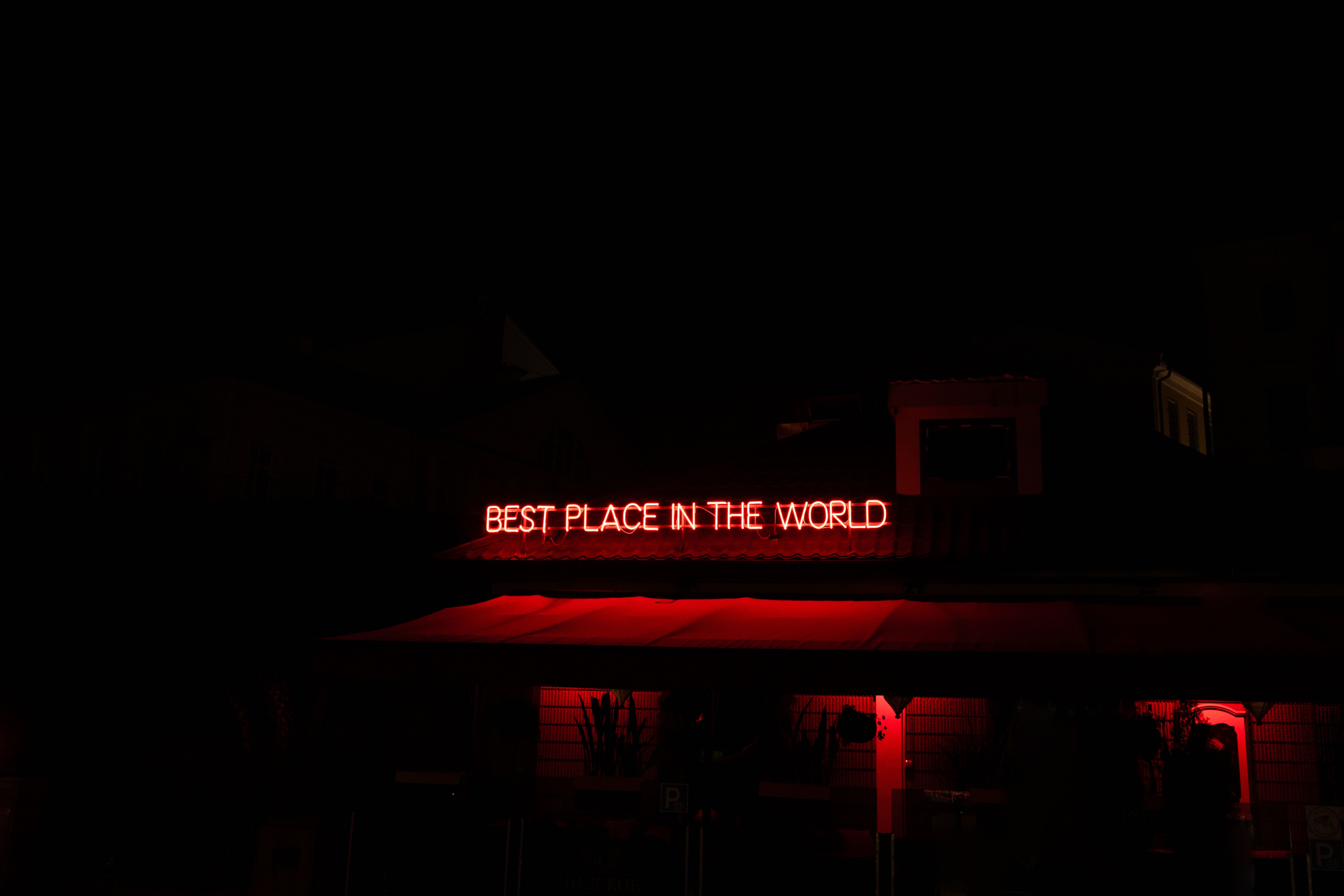 Red neon sign glowing against a dark building facade at night.